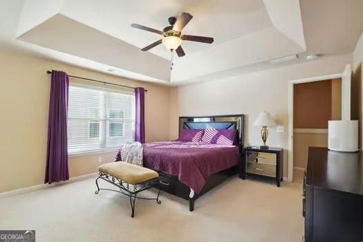 bedroom featuring light colored carpet, ceiling fan, and a tray ceiling