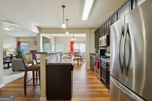 kitchen featuring appliances with stainless steel finishes, pendant lighting, a breakfast bar area, dark brown cabinetry, and a center island with sink