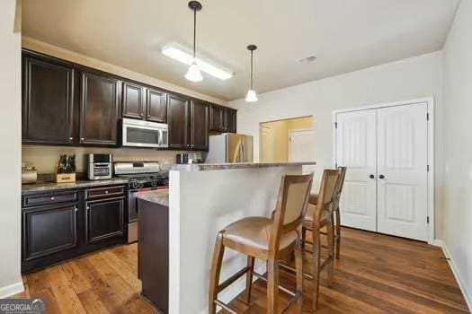 kitchen with a breakfast bar, hanging light fixtures, stainless steel appliances, dark brown cabinets, and a center island with sink