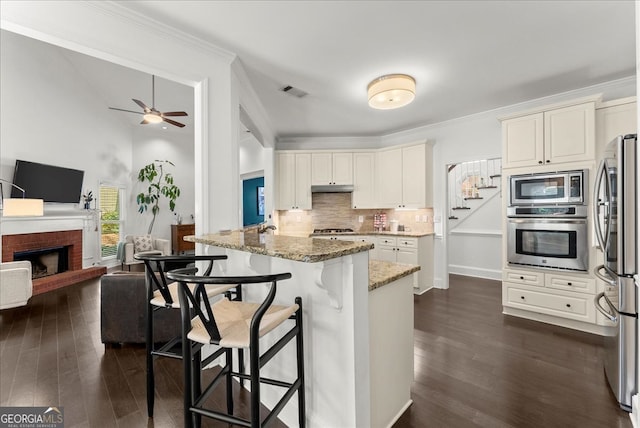 kitchen with appliances with stainless steel finishes, backsplash, light stone counters, white cabinets, and a kitchen bar