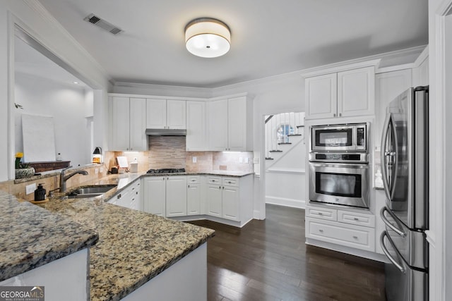 kitchen with appliances with stainless steel finishes, white cabinetry, sink, dark stone countertops, and kitchen peninsula