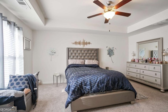 carpeted bedroom featuring multiple windows, a tray ceiling, and ceiling fan