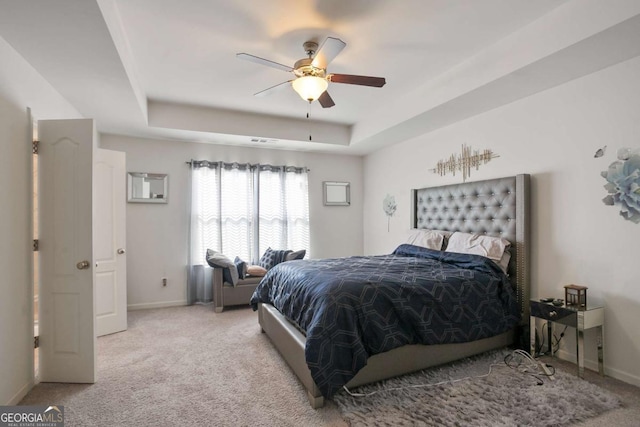 carpeted bedroom with ceiling fan and a tray ceiling