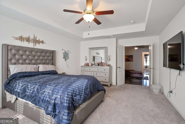 bedroom with light colored carpet, a raised ceiling, and ceiling fan