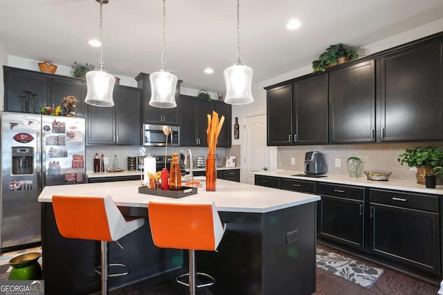 kitchen with stainless steel appliances, hanging light fixtures, a center island with sink, and backsplash