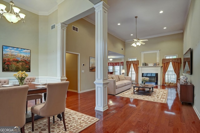 interior space featuring wood-type flooring, a high ceiling, ornamental molding, ceiling fan with notable chandelier, and decorative columns