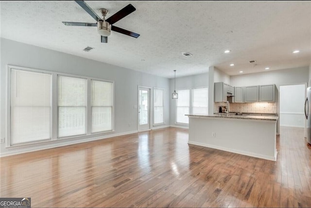 kitchen with backsplash, light wood-type flooring, a kitchen island with sink, gray cabinetry, and a textured ceiling