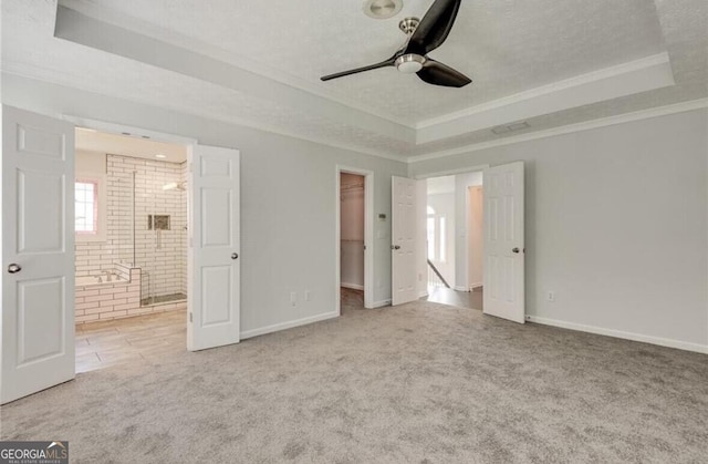 unfurnished bedroom featuring ceiling fan, light colored carpet, a tray ceiling, and a walk in closet