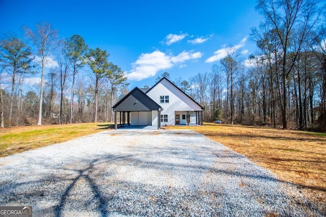 view of front facade featuring covered porch, a view of trees, a carport, driveway, and a front lawn