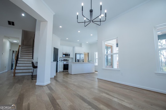 unfurnished living room with a high ceiling, crown molding, a notable chandelier, and light wood-type flooring