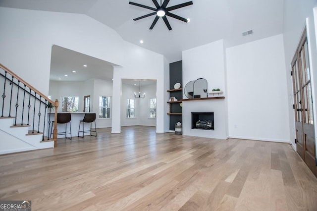 unfurnished living room featuring a fireplace, visible vents, wood finished floors, high vaulted ceiling, and stairs