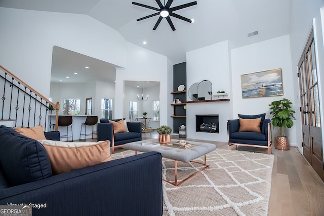 living area featuring high vaulted ceiling, a fireplace, wood finished floors, visible vents, and an inviting chandelier