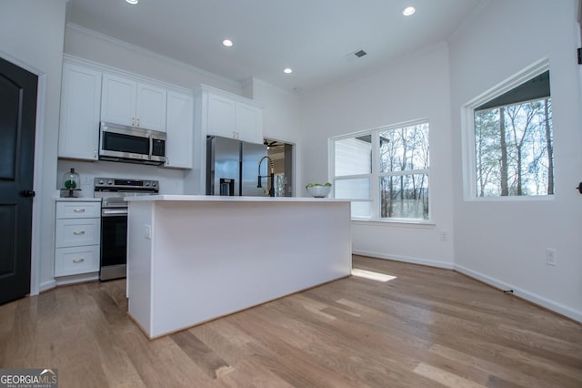 kitchen with white cabinets, light wood-type flooring, appliances with stainless steel finishes, and an island with sink