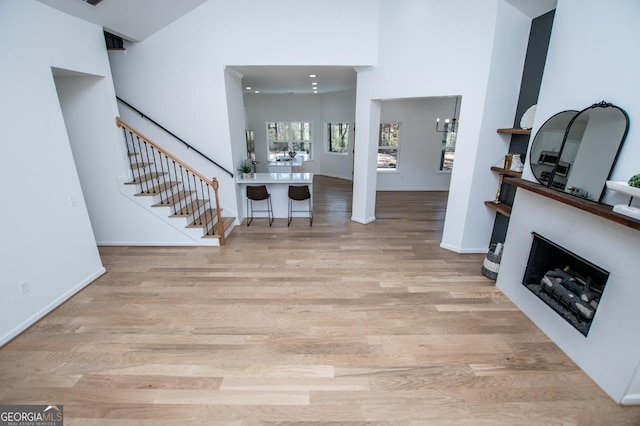 entrance foyer featuring a fireplace, a high ceiling, wood finished floors, baseboards, and stairs