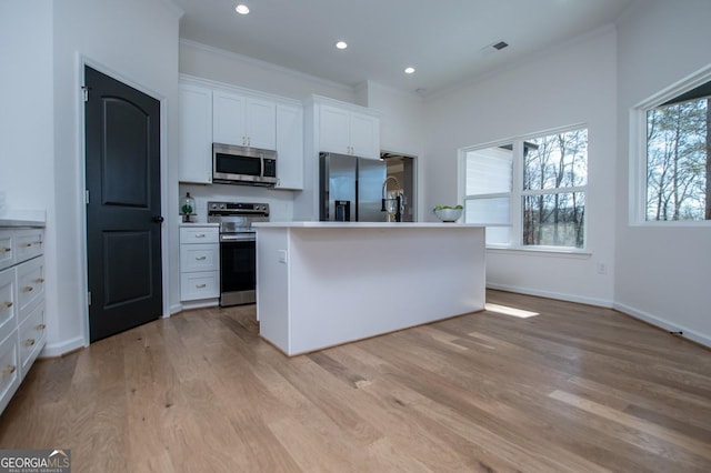 kitchen with a center island with sink, stainless steel appliances, light hardwood / wood-style flooring, and white cabinets