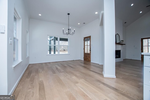 unfurnished dining area with a notable chandelier, a fireplace, recessed lighting, light wood-style floors, and baseboards