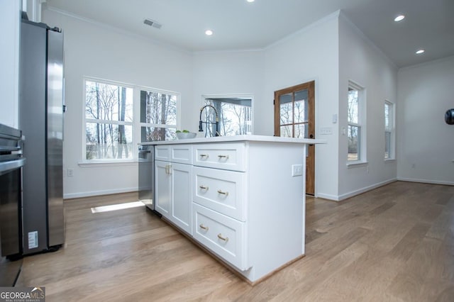 kitchen with a wealth of natural light, white cabinets, crown molding, and an island with sink