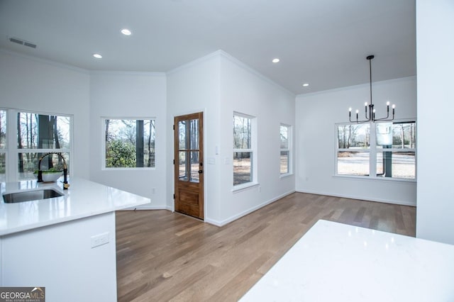 kitchen featuring wood-type flooring, sink, hanging light fixtures, a chandelier, and crown molding