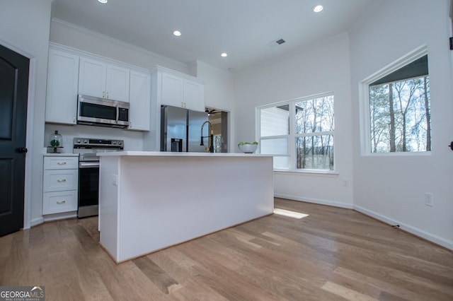 kitchen with stainless steel appliances, light wood-type flooring, white cabinets, and a healthy amount of sunlight