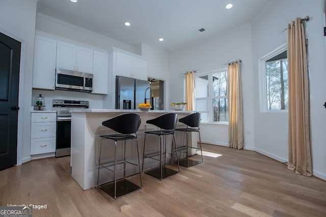 kitchen with stainless steel appliances, light wood-type flooring, white cabinets, and a center island with sink