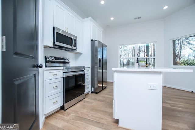 kitchen with white cabinets, an island with sink, appliances with stainless steel finishes, ornamental molding, and a sink