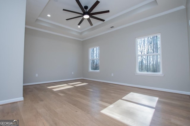 empty room with ornamental molding, a raised ceiling, baseboards, and wood finished floors