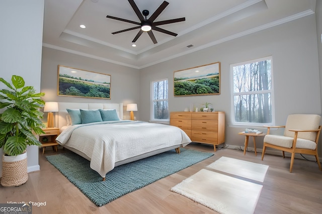 bedroom with light wood-style flooring, a raised ceiling, and crown molding