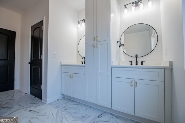 full bath with marble finish floor, a sink, baseboards, and double vanity