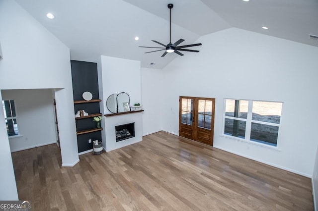 living room featuring high vaulted ceiling, recessed lighting, a fireplace, wood finished floors, and french doors