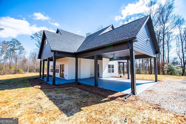 view of side of property with a ceiling fan, a patio area, a yard, and roof with shingles