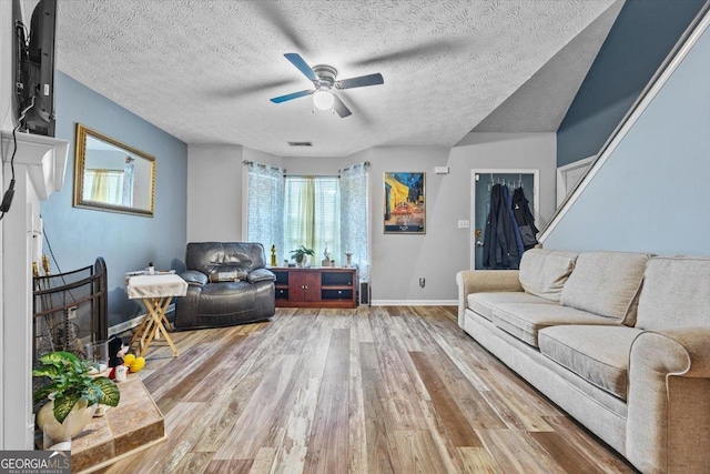 living room with a textured ceiling, ceiling fan, and wood-type flooring