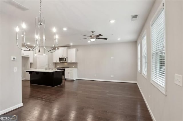 kitchen featuring appliances with stainless steel finishes, white cabinetry, backsplash, hanging light fixtures, and a center island with sink