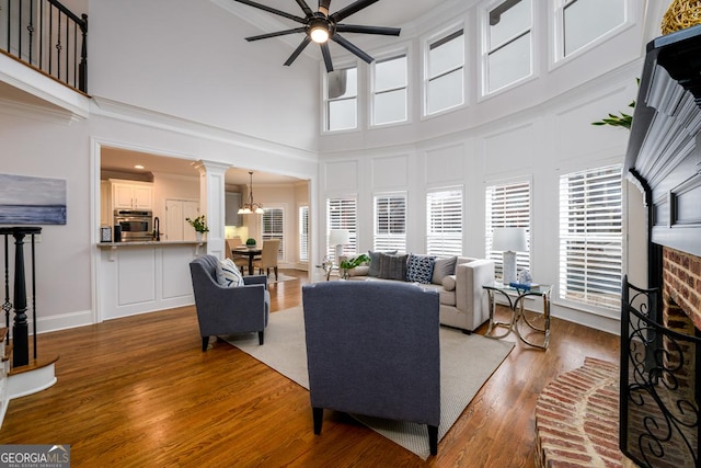 living room with a fireplace, ceiling fan with notable chandelier, a high ceiling, and ornate columns