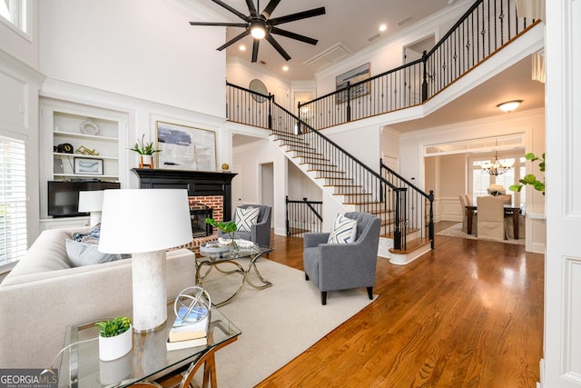 living room featuring a brick fireplace, hardwood / wood-style floors, built in features, and a towering ceiling