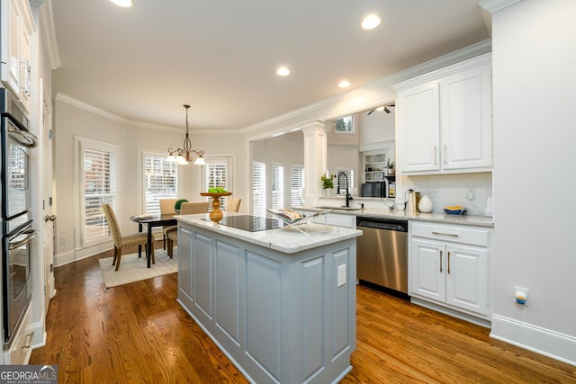 kitchen featuring white cabinets, appliances with stainless steel finishes, a kitchen island, decorative light fixtures, and crown molding