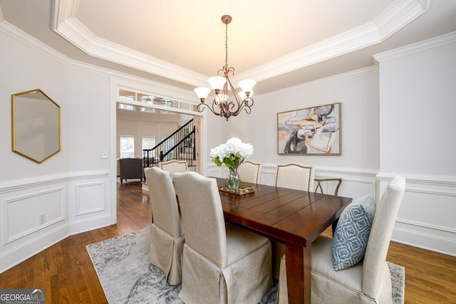 dining area featuring ornamental molding, dark wood-type flooring, a tray ceiling, and an inviting chandelier