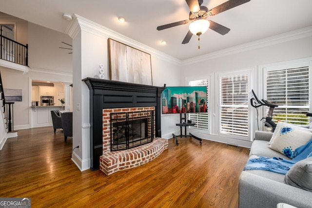 living room featuring a brick fireplace, dark wood-type flooring, crown molding, and ceiling fan