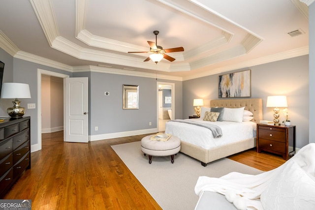 bedroom with ceiling fan, hardwood / wood-style flooring, a tray ceiling, and ornamental molding