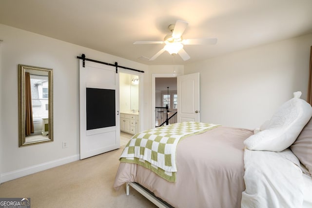 bedroom featuring ceiling fan, light carpet, ensuite bathroom, and a barn door