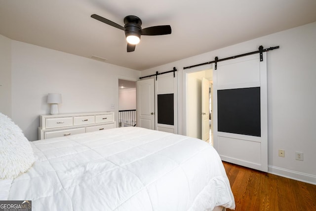 bedroom with ceiling fan, dark hardwood / wood-style floors, and a barn door