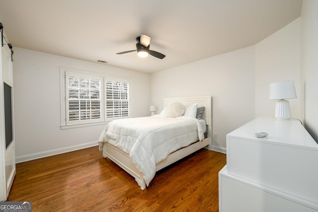 bedroom featuring dark wood-type flooring, ceiling fan, and a barn door