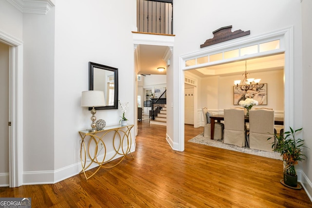 hall with wood-type flooring, a towering ceiling, a notable chandelier, and ornamental molding