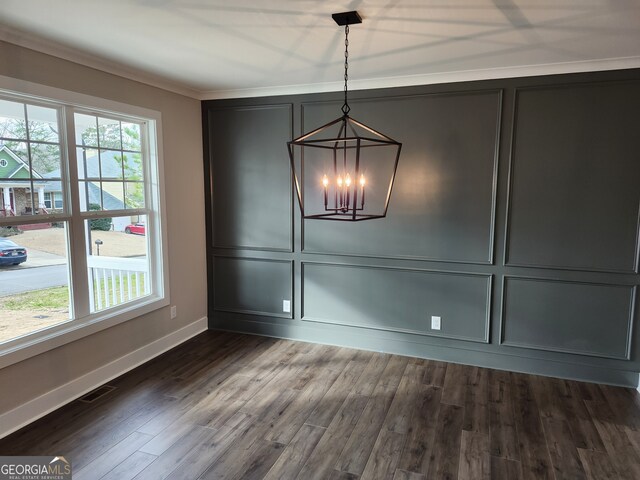 unfurnished dining area featuring dark wood-type flooring, plenty of natural light, crown molding, and a chandelier