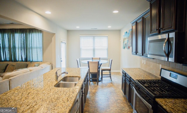 kitchen with appliances with stainless steel finishes, sink, decorative backsplash, light stone counters, and dark brown cabinets