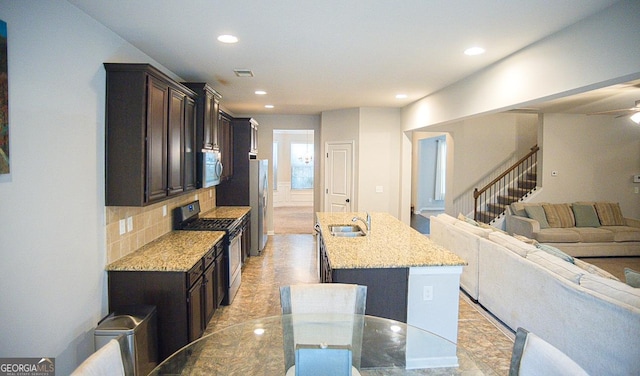 kitchen featuring sink, appliances with stainless steel finishes, a kitchen island with sink, backsplash, and light stone countertops