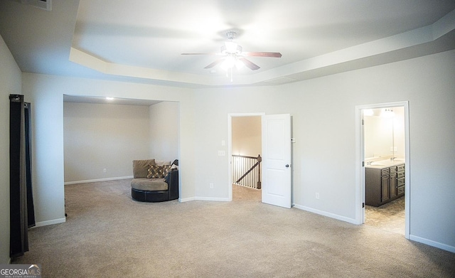 living area with ceiling fan, a tray ceiling, and light carpet