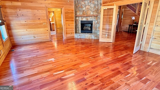 unfurnished living room with a stone fireplace, wood finished floors, and wooden walls