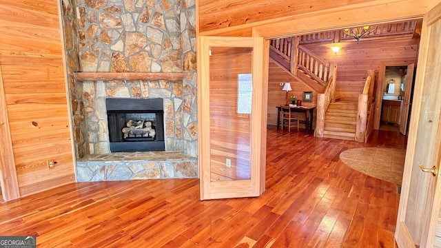 unfurnished living room with a stone fireplace, wood walls, stairway, and wood finished floors