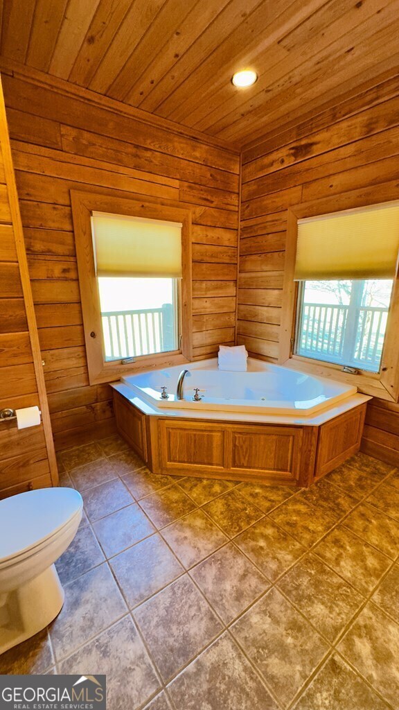 bathroom featuring toilet, tile patterned floors, a bathing tub, wooden walls, and wood ceiling