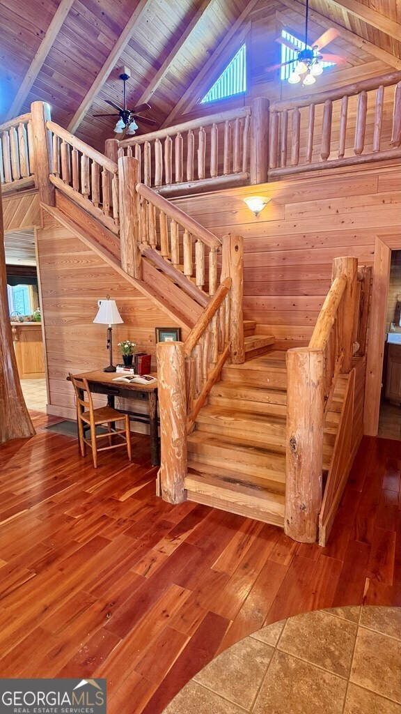 stairway with ceiling fan, hardwood / wood-style flooring, wooden walls, and beamed ceiling